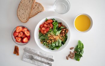 Top view of a healthy salad and fresh ingredients with bread and juice on a white surface.